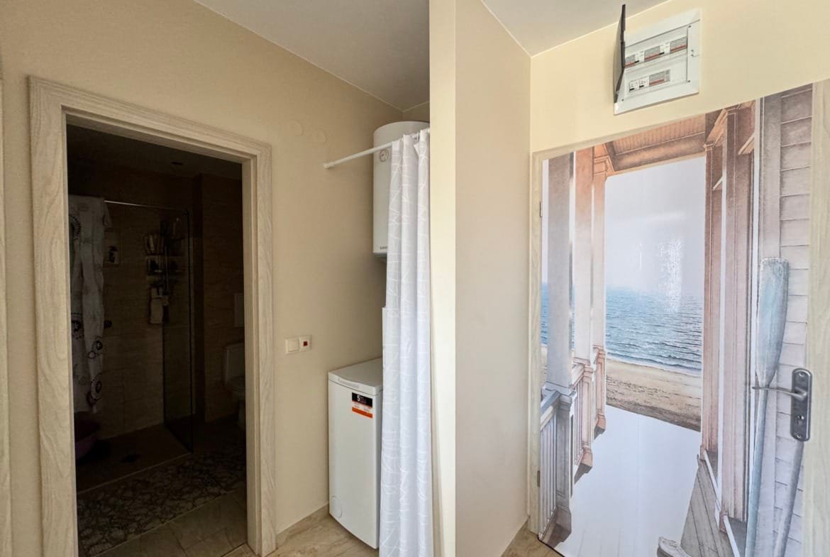 Современный интерьер ванной комнаты с холодильником и стеной с дверью, ведущей к морскому пейзажу. Купить жилье в Болгарии.