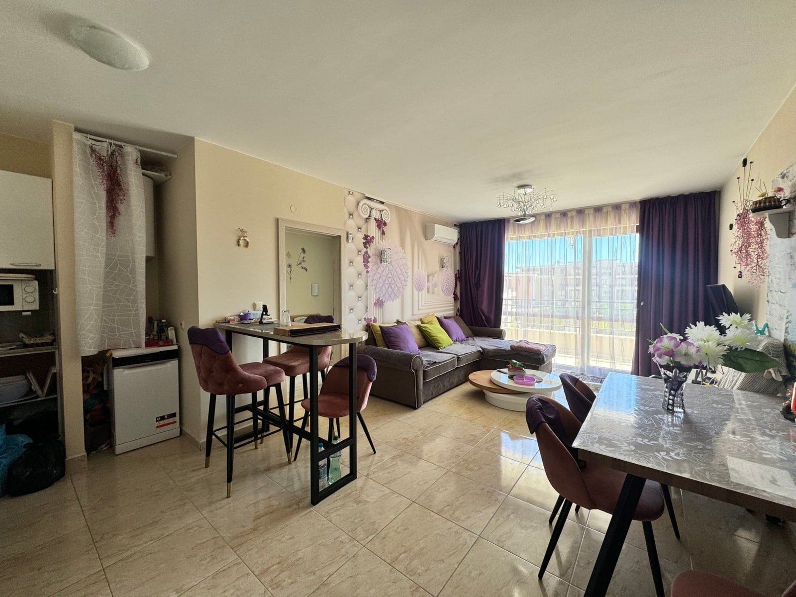 Современный интерьер квартиры с открытым планом и балконом Современная квартира в Болгарии с светлым интерьером, зоной отдыха и обеденной зоной, открывающей вид на улицу.