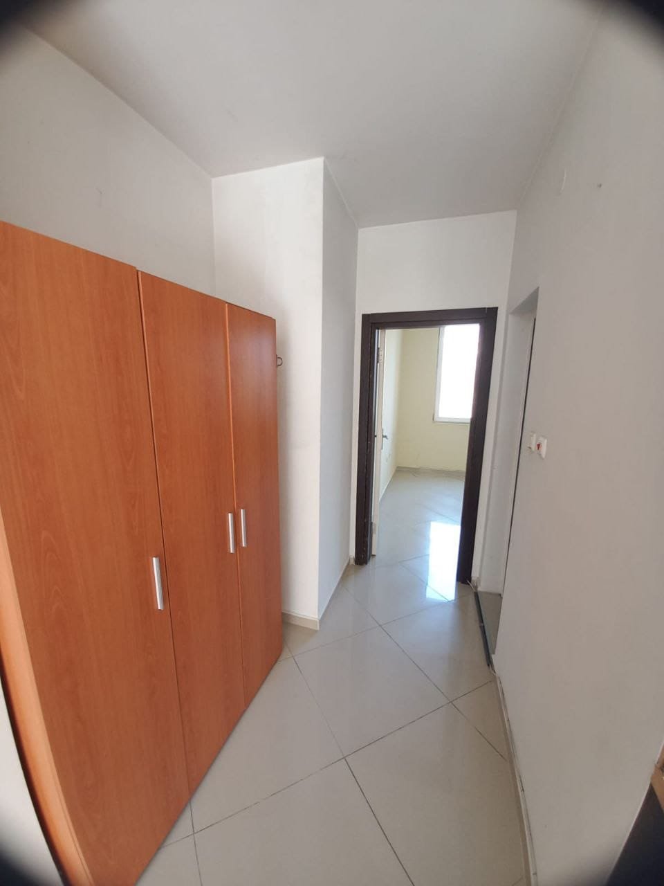 Современный коридор с деревянным шкафом и светлыми стенами Современный коридор с деревянным шкафом, плиточным полом и светлыми стенами, идеально подходящий для покупки недвижимости в Болгарии.