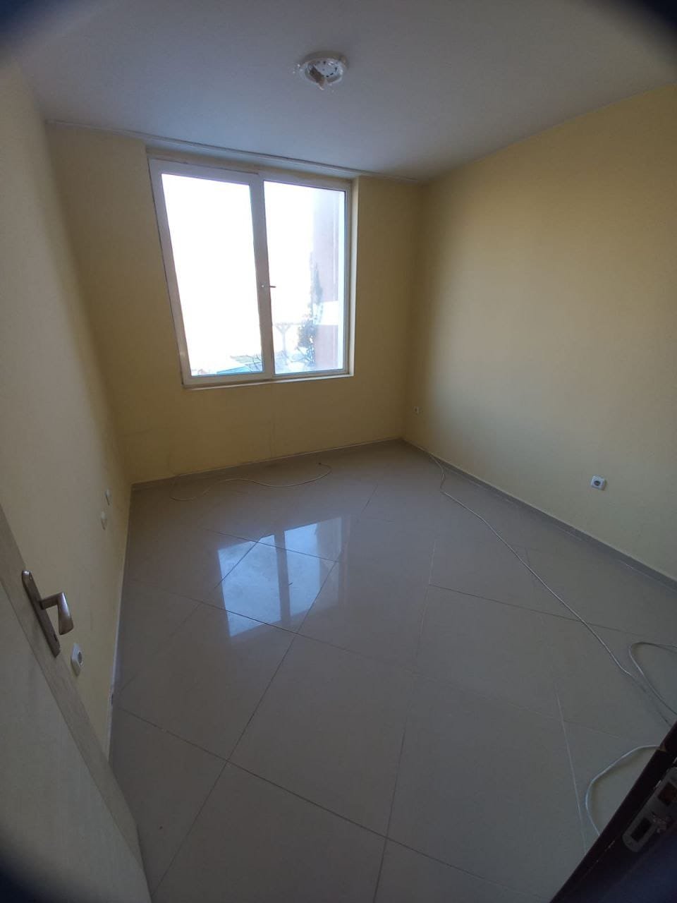 Пустая комната с окнами, свежим ремонтом и плиточным полом Светлая комната с желтыми стенами и большой окном, готовая к продаже или аренде в Болгарии. Полы выполнены из плитки.