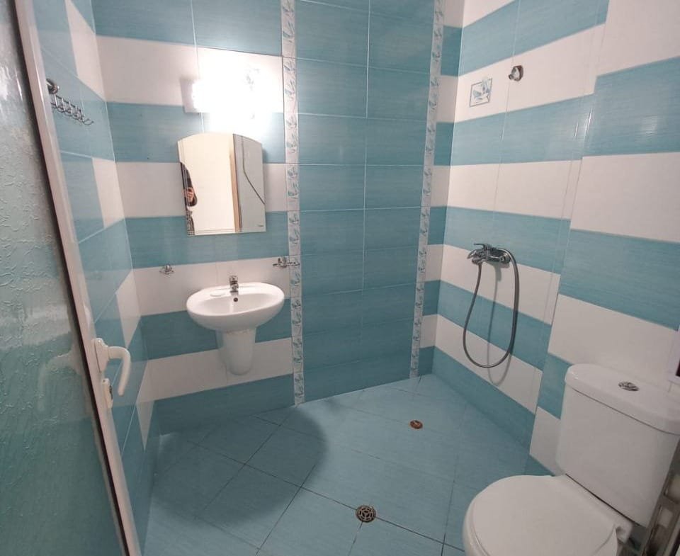 Светлая ванная комната с голубыми и белыми полосами, умывальником, душем и туалетом, готовая для продажи недвижимости в Болгарии.