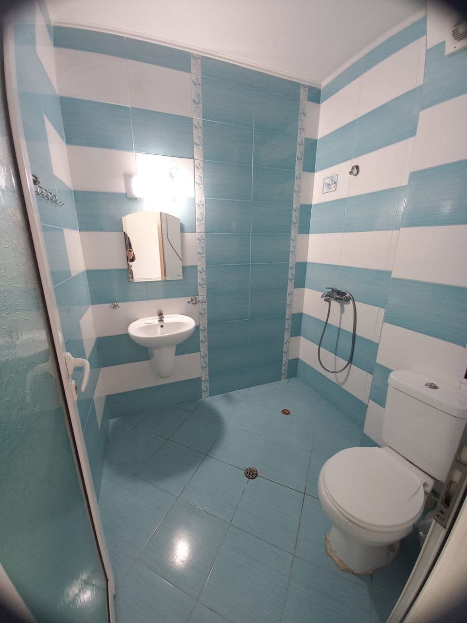 Современная ванная комната с голубыми стенами и сантехникой Светлая ванная комната с голубыми и белыми полосами, умывальником, душем и туалетом, готовая для продажи недвижимости в Болгарии.