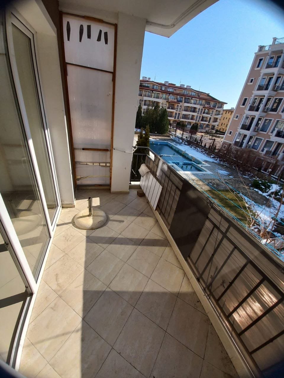 Балкон с видом на бассейн и парк в жилом комплексе Балкон с плиточным полом и панорамным видом на бассейн в жилом комплексе в Болгарии. Чистое небо и зелень в окрестностях.