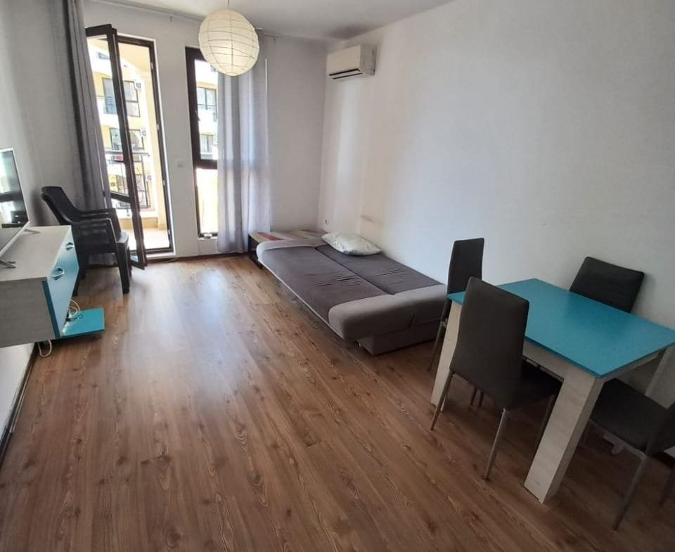 Современная квартира в Болгарии, светлая гостиная с деревянным полом, диван, стол и стулья, балкон с видом.