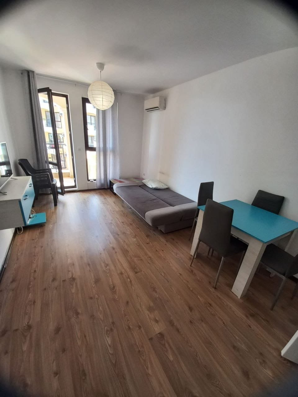 Современная квартира в светлых тонах с мебелью и балконом Современная квартира в Болгарии, светлая гостиная с деревянным полом, диван, стол и стулья, балкон с видом.