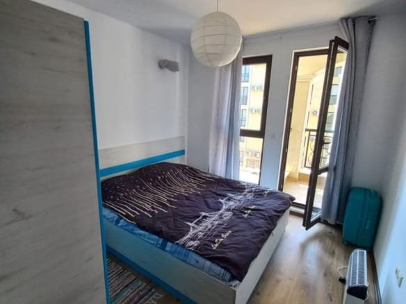 Современная светлая спальня с двуспальной кроватью, балконом и уютным интерьером в Болгарии для покупки недвижимости.