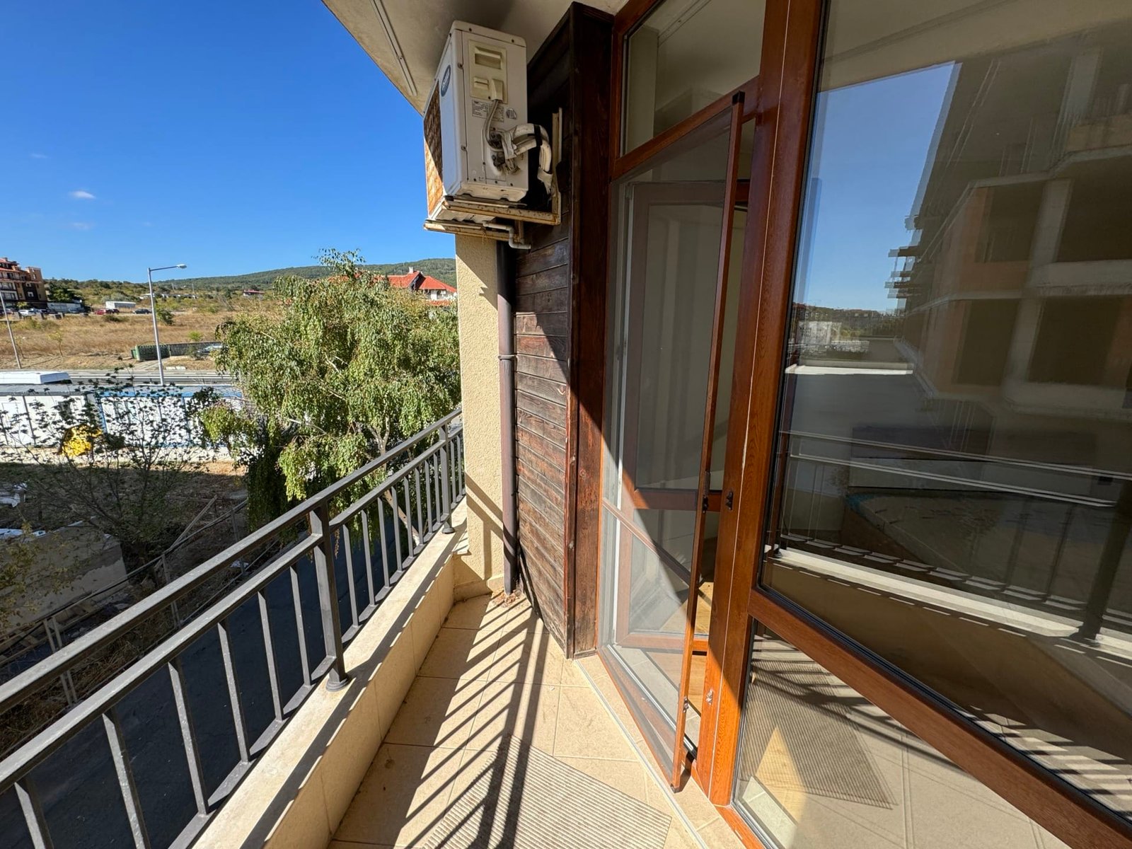 Балкон с кондиционером и видом на окрестности. Балкон с стеклянной дверью, открывающей вид на окрестности, идеальное место для покупки недвижимости в Болгарии.