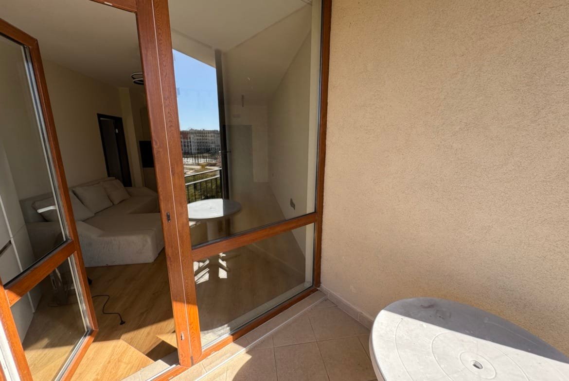 Балкон с столиком, выходящий на светлую комнату. Предлагает вид на пейзаж и пространство для отдыха в недвижимости в Болгарии.