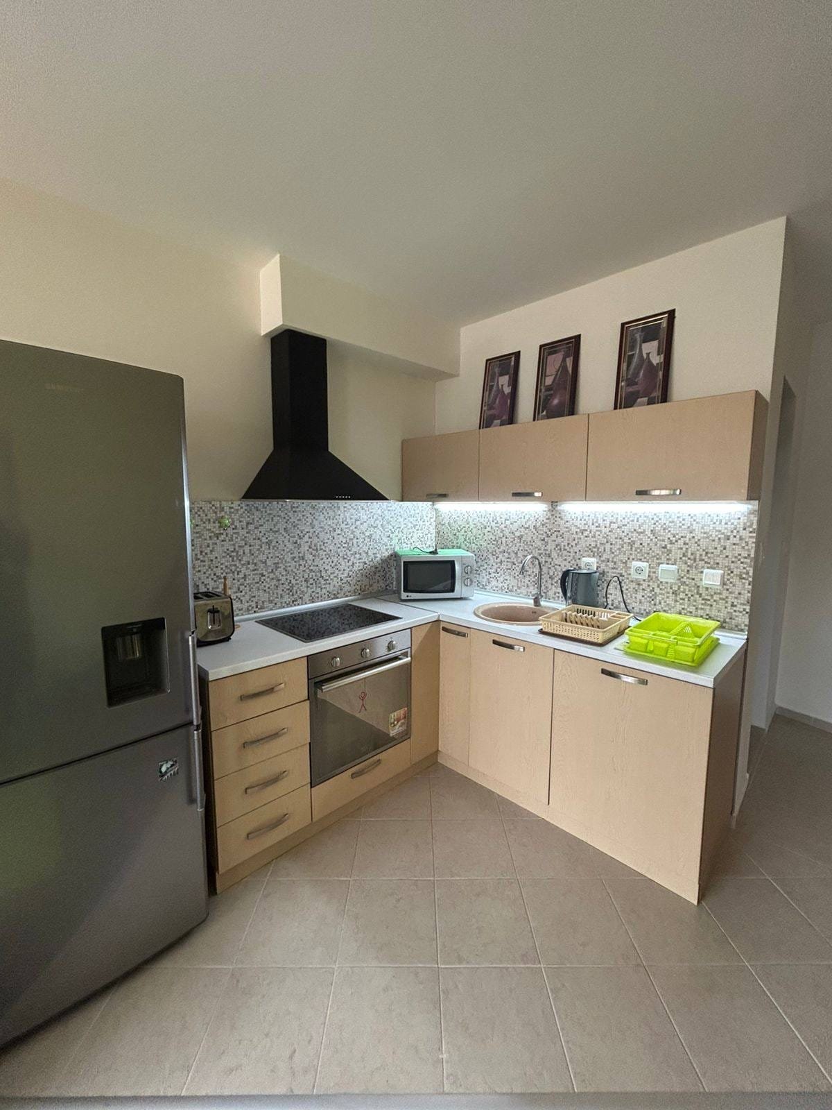 Современная кухня с металлической техникой и стильным дизайном Современная кухня с холодильником, плитой и светлым зеленым аксессуаром, идеальная для покупки недвижимости в Болгарии.