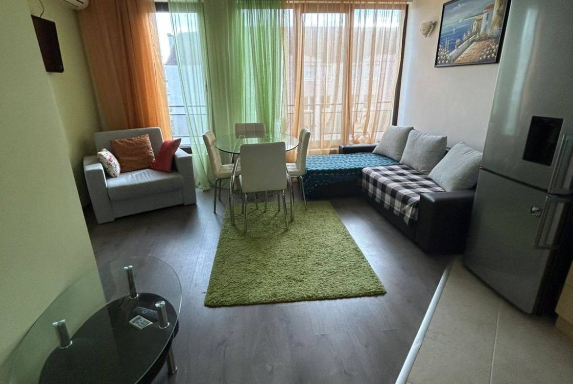 Современная гостиная в квартире в Болгарии с обеденной зоной, диваном и большими окнами, создающими светлую атмосферу.