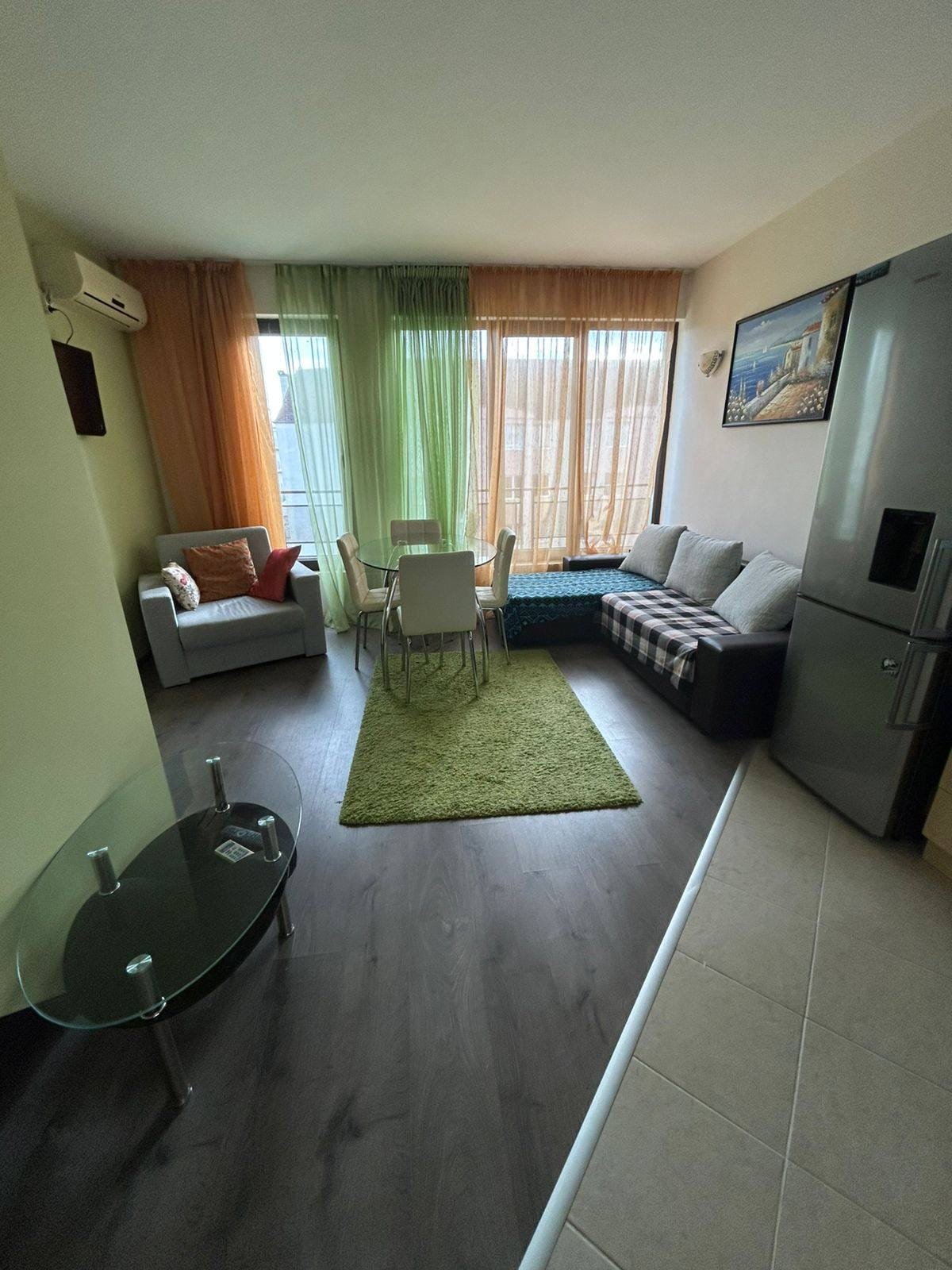 Современная квартира с уютной гостиной и обеденной зоной. Современная гостиная в квартире в Болгарии с обеденной зоной, диваном и большими окнами, создающими светлую атмосферу.