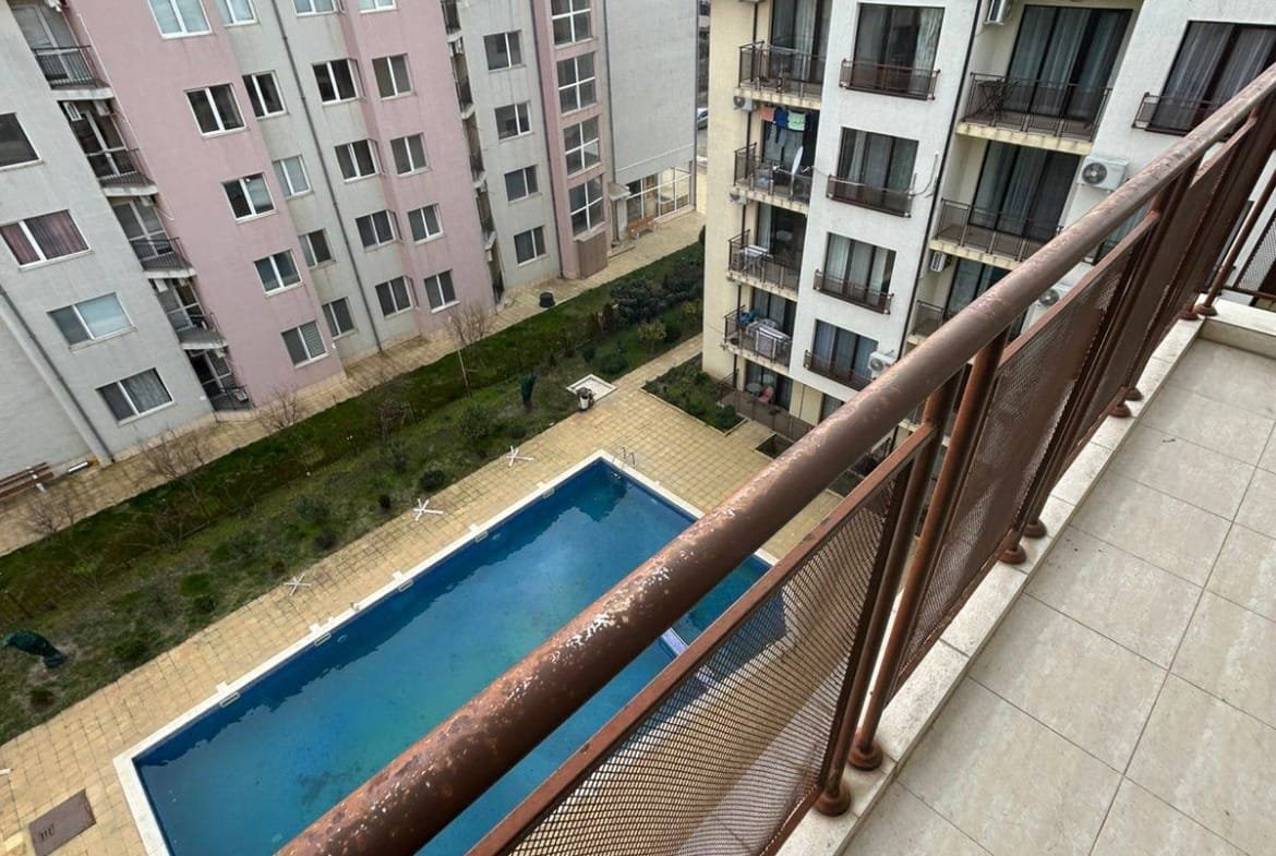 Балкон с видом на общее пространство и бассейн жилого комплекса в Болгарии, окружённого многоэтажными домами.