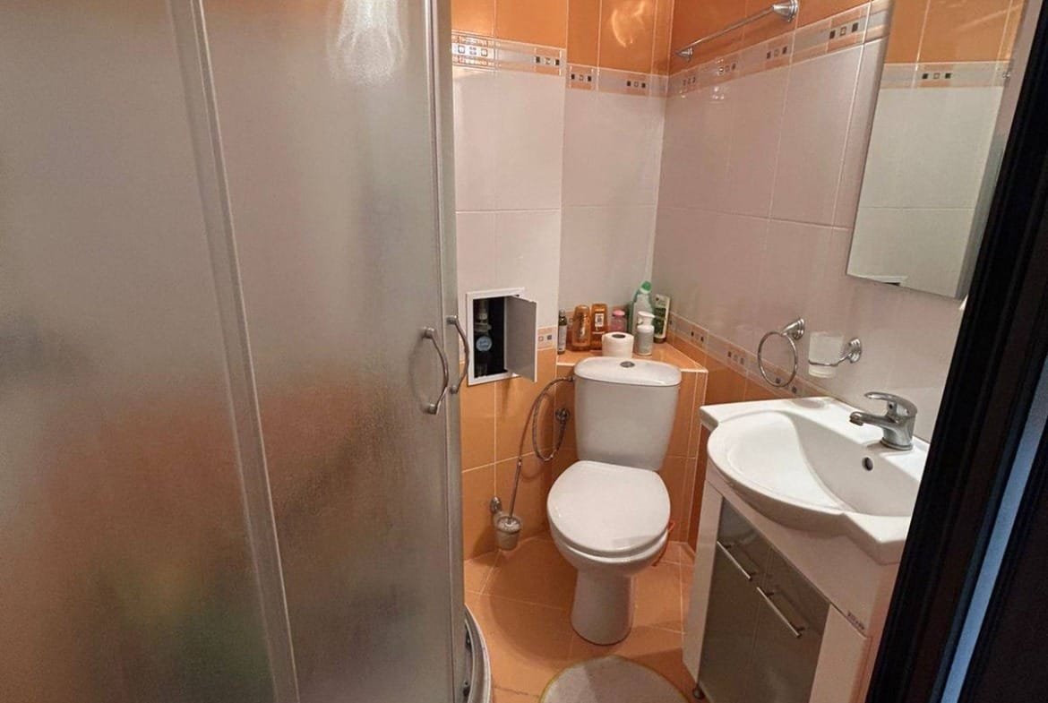 Современная ванная комната с душевой кабиной, унитазом и раковиной, оформленная в теплых оранжевых тонах.