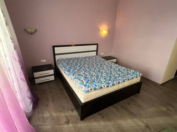 Современная спальня с кроватью, комодом и мягкими шторами пурпурного цвета, идеальна для аренды недвижимости в Болгарии.