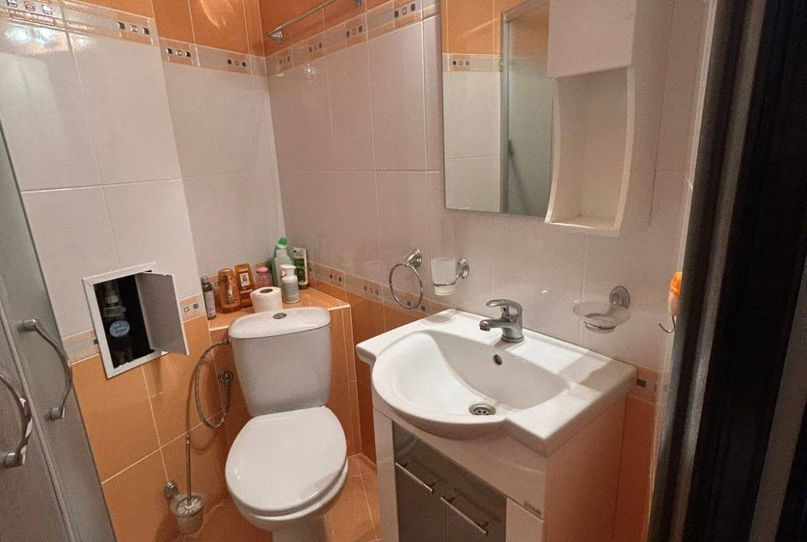 Современная ванная комната с душевой кабиной, унитазом и раковиной, отделка в оранжевых и белых тонах, подходящая для продажи недвижимости в Болгарии.