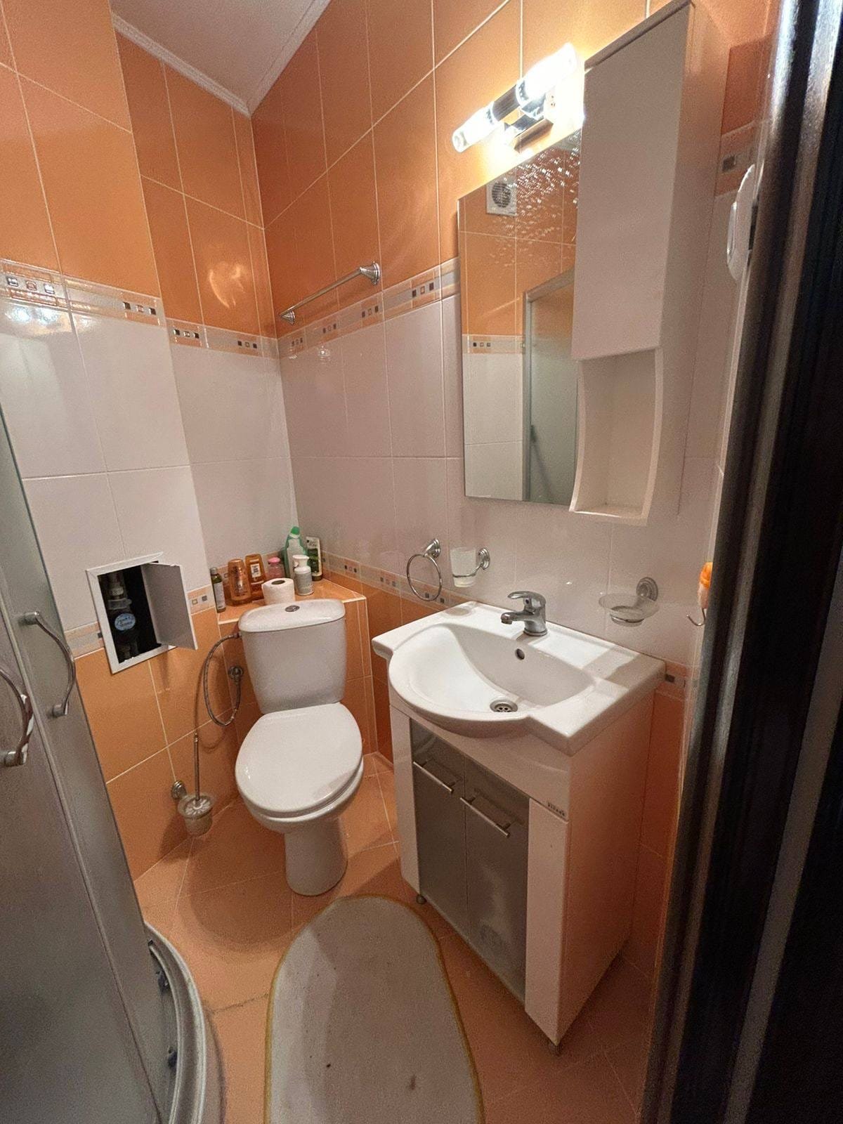 Современная ванная комната с душевой сеткой и современными аксессуарами Современная ванная комната с душевой кабиной, унитазом и раковиной, отделка в оранжевых и белых тонах, подходящая для продажи недвижимости в Болгарии.