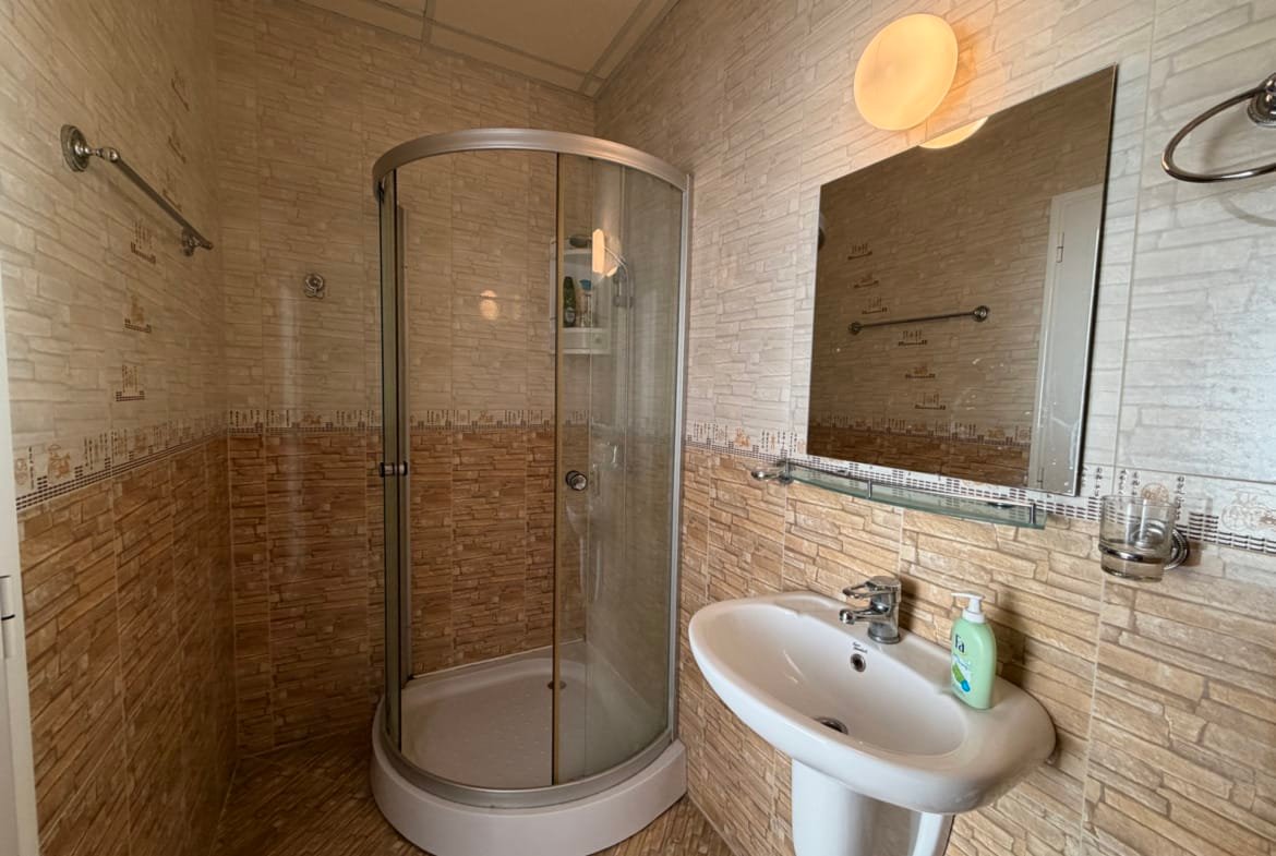 Современная ванная комната в недвижимости Болгарии с душевой кабиной, умывальником и стильной отделкой стен.