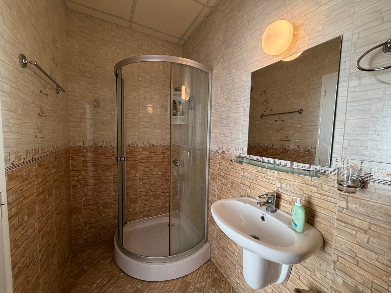 Современная ванная комната в недвижимости Болгарии с душевой кабиной, умывальником и стильной отделкой стен.