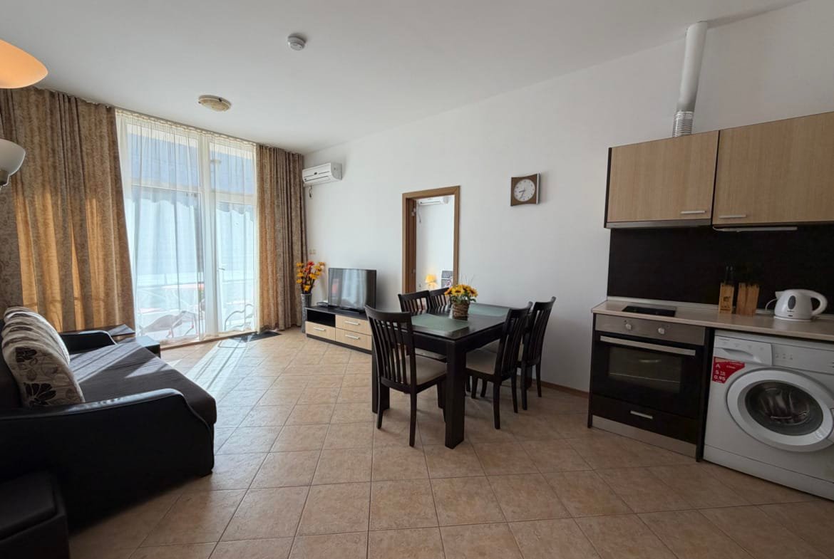 Современная квартира в Болгарии с оборудованной кухней, обеденной зоной, диваном и балконом, идеальна для отдыха.