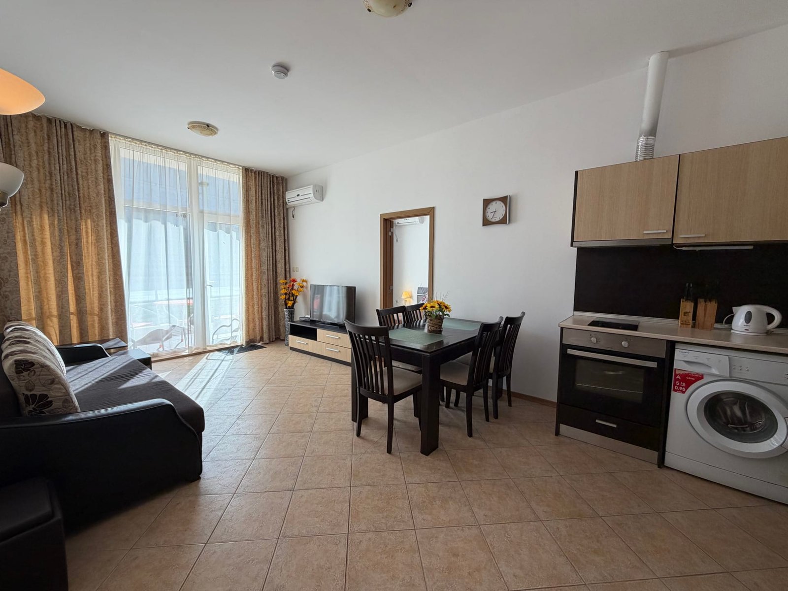 Современная квартира в Болгарии с оборудованной кухней, обеденной зоной, диваном и балконом, идеальна для отдыха.