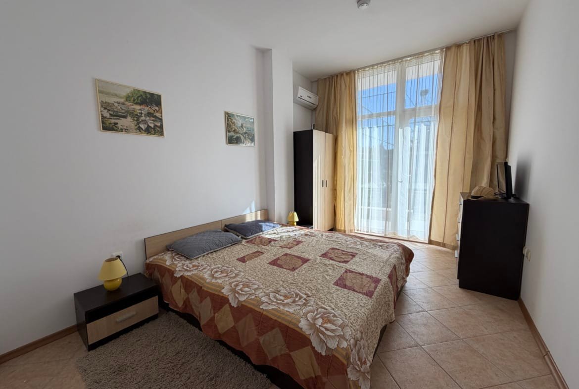 Современная спальня с двуспальной кроватью, светлыми шторами и выходом на балкон в квартире в Болгарии.