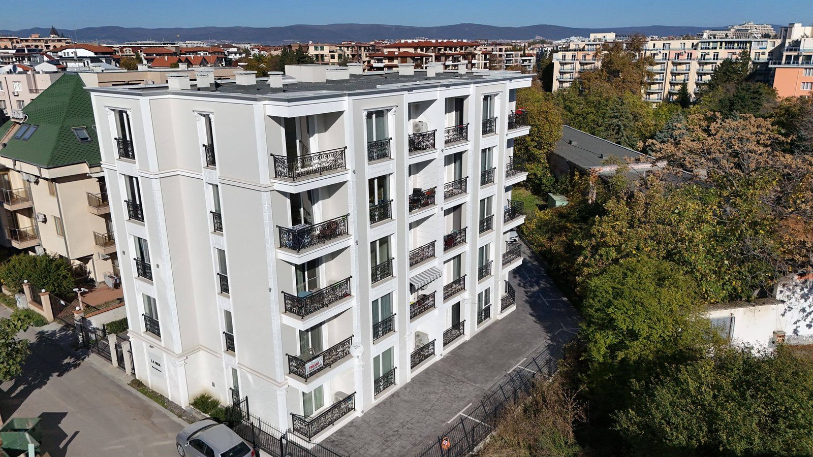 Современное здание с балконами, окруженное зеленью и городскими жилыми кварталами, расположенное в комплексе La Mer Gold.