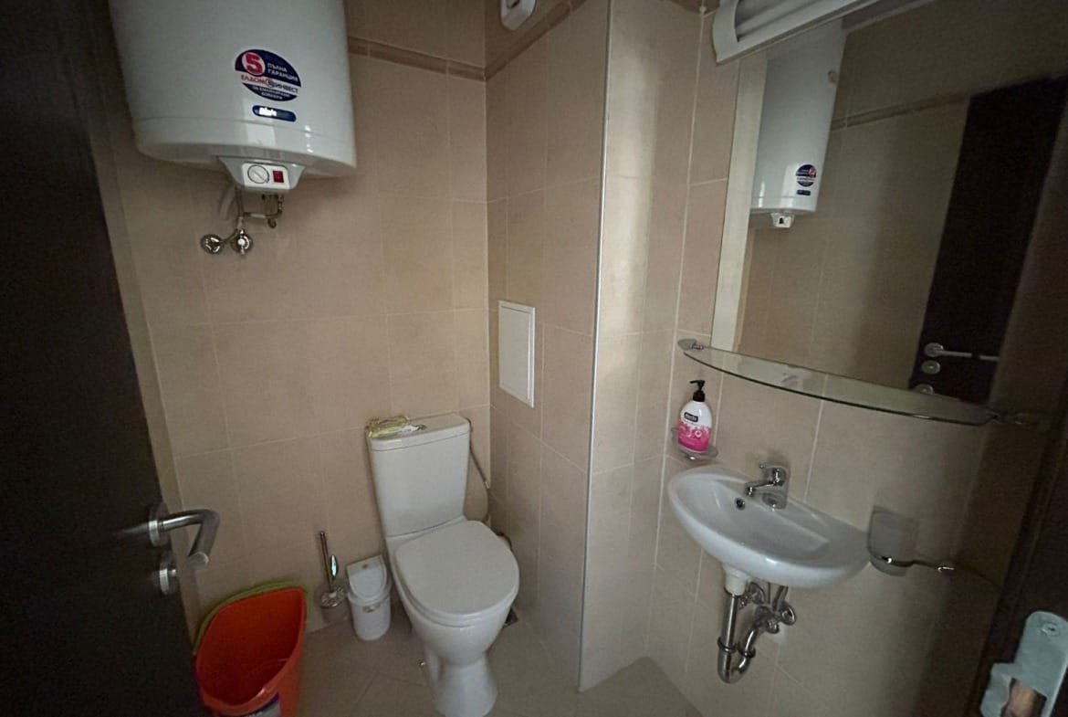 Современный санузел с унитазом, раковиной и зеркалом, отделка в светлых тонах, подходящий для жилья в Болгарии.