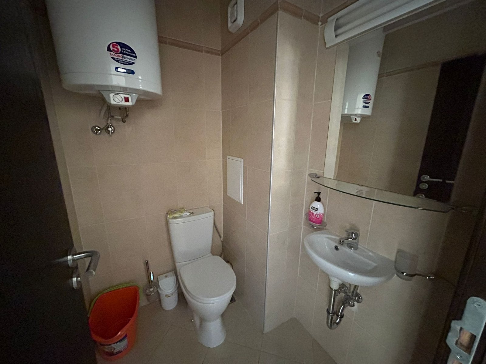 Уютная ванная комната с унитазом и раковиной в современном стиле. Современный санузел с унитазом, раковиной и зеркалом, отделка в светлых тонах, подходящий для жилья в Болгарии.