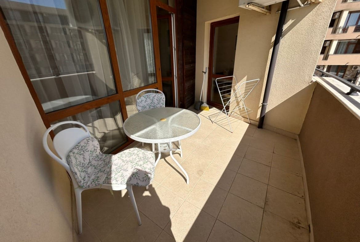 Балкон с круглым столом и стульями, на полу плитка, освещён солнечным светом, идеальное место для отдыха в Болгарии.