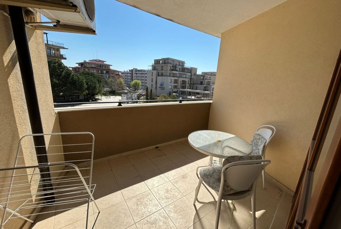 Балкон с круглым стеклянным столом и стульями, вид на городские здания в Болгарии, идеальное место для отдыха.