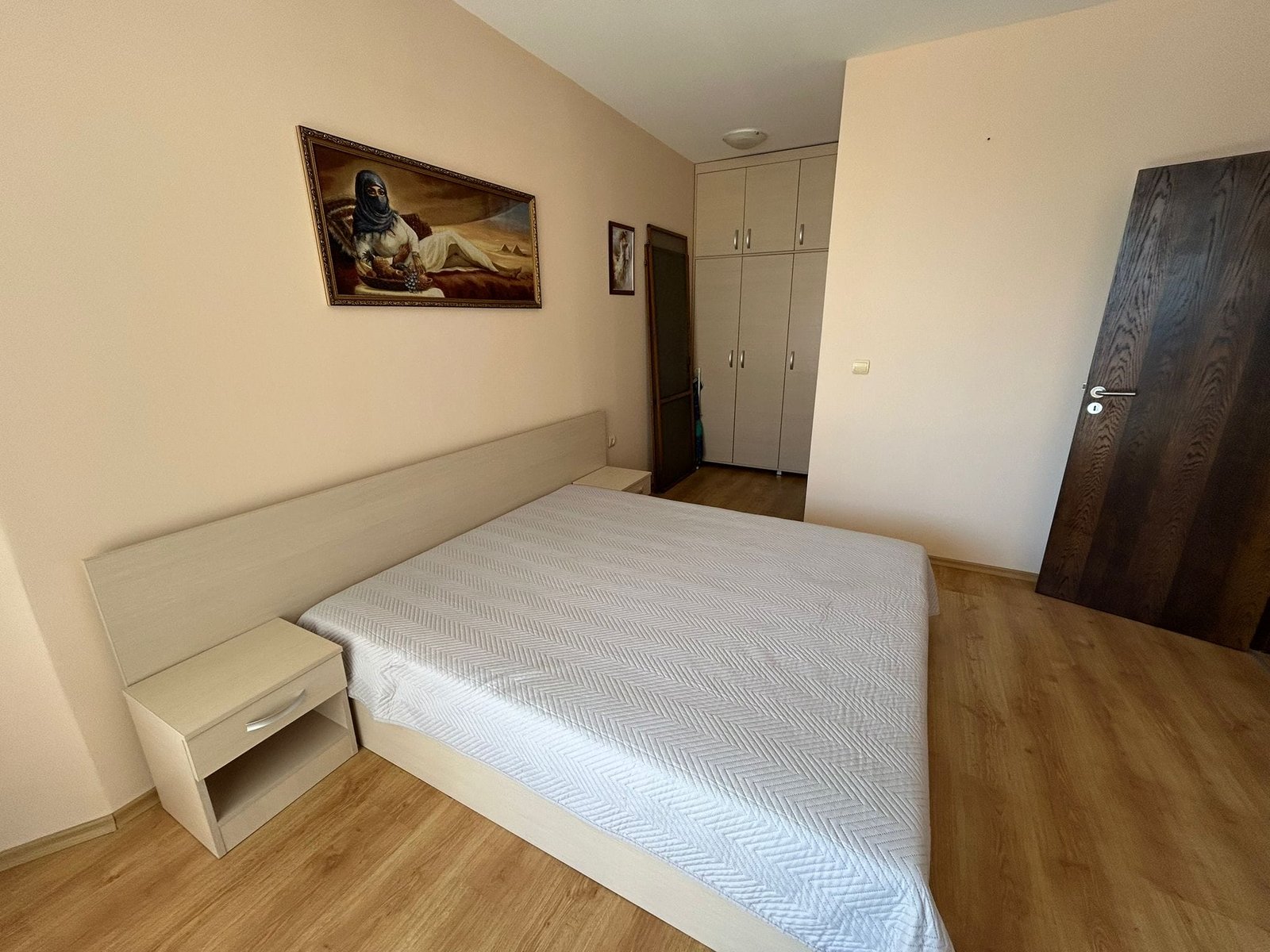 Современная спальня с светлым интерьером и деревянным полом Современная спальня с двуспальной кроватью, светлыми стенами и шкафом, предназначенная для продажи недвижимости в Болгарии.