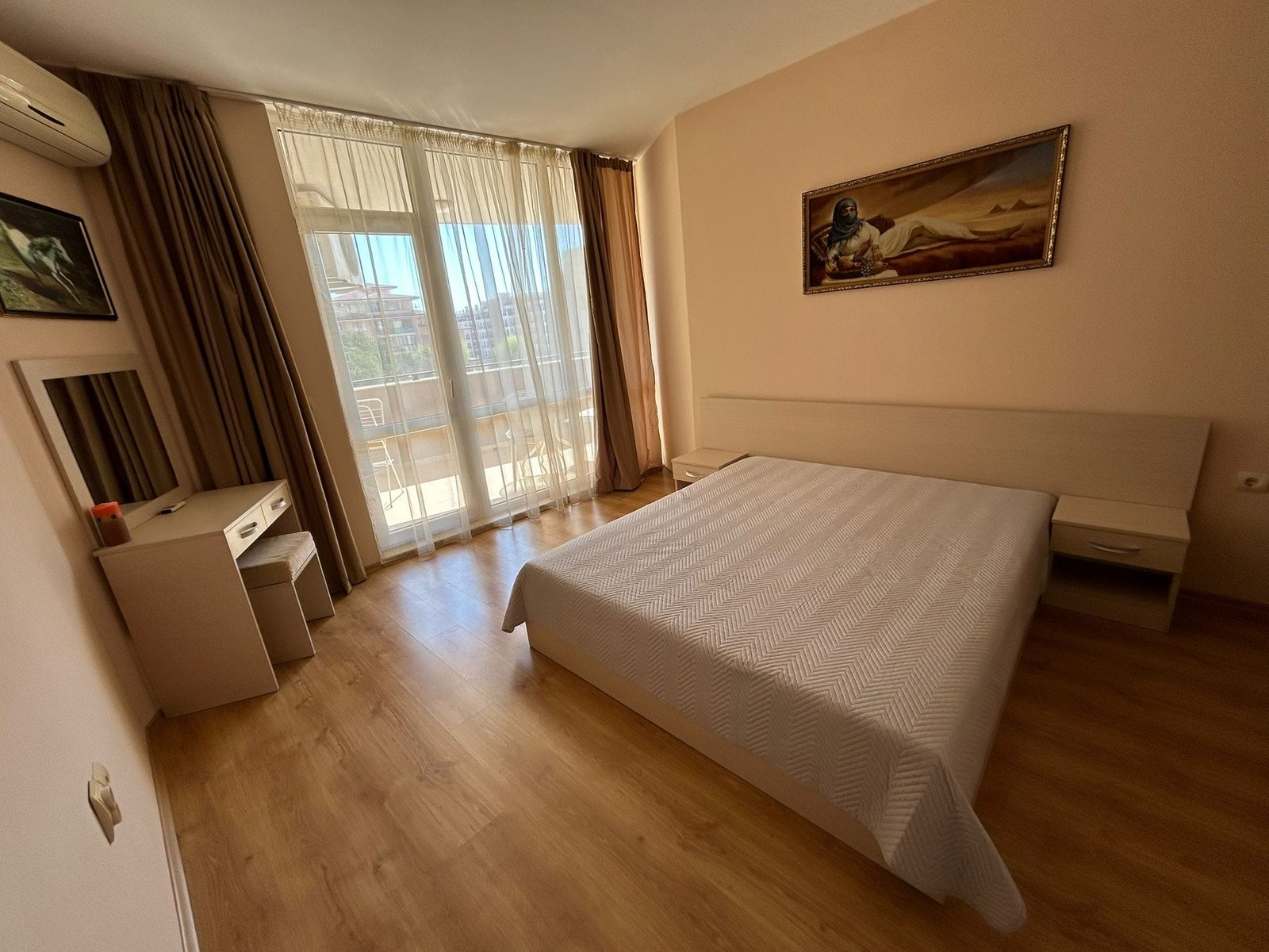 Современная спальня с балконом и натуральным освещением Современная спальня с двуспальной кроватью, светлым интерьером и большим окном, выходящим на балкон в Болгарии.