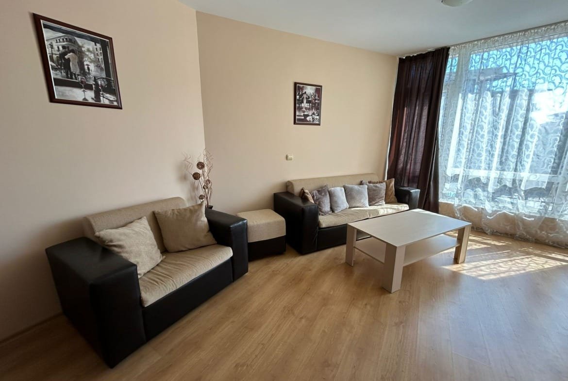 Светлая гостиная с мягкой мебелью, столом и занавесками, подходит для продажи или аренды недвижимости в Болгарии.