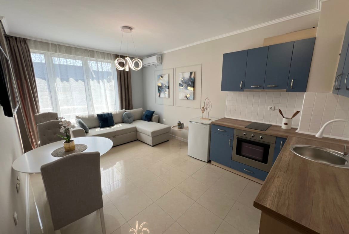 Современная гостиная с кухонным уголком, светлыми тонами и уютной мебелью, идеально подходит для покупки недвижимости в Болгарии.