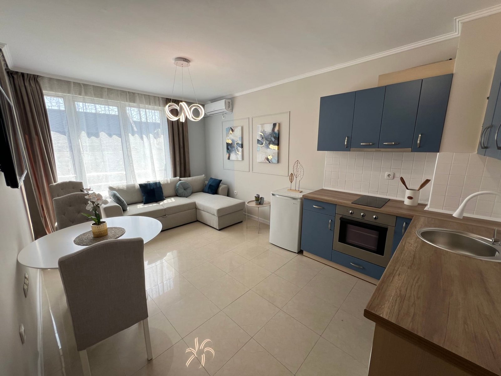 Современная гостиная с кухонным уголком, светлыми тонами и уютной мебелью, идеально подходит для покупки недвижимости в Болгарии.