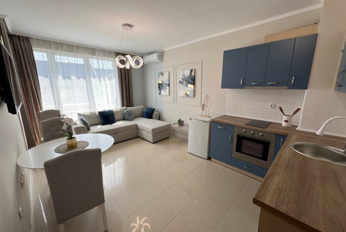 Современный интерьер квартиры в Болгарии с уютной гостиной, кухонным блоком, светлыми тонами и большими окнами.