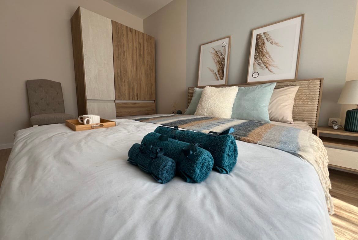 Современная спальня с уютной кроватью, декоративными подушками и стильными картинами, интерьер подходит для жилья в Болгарии.