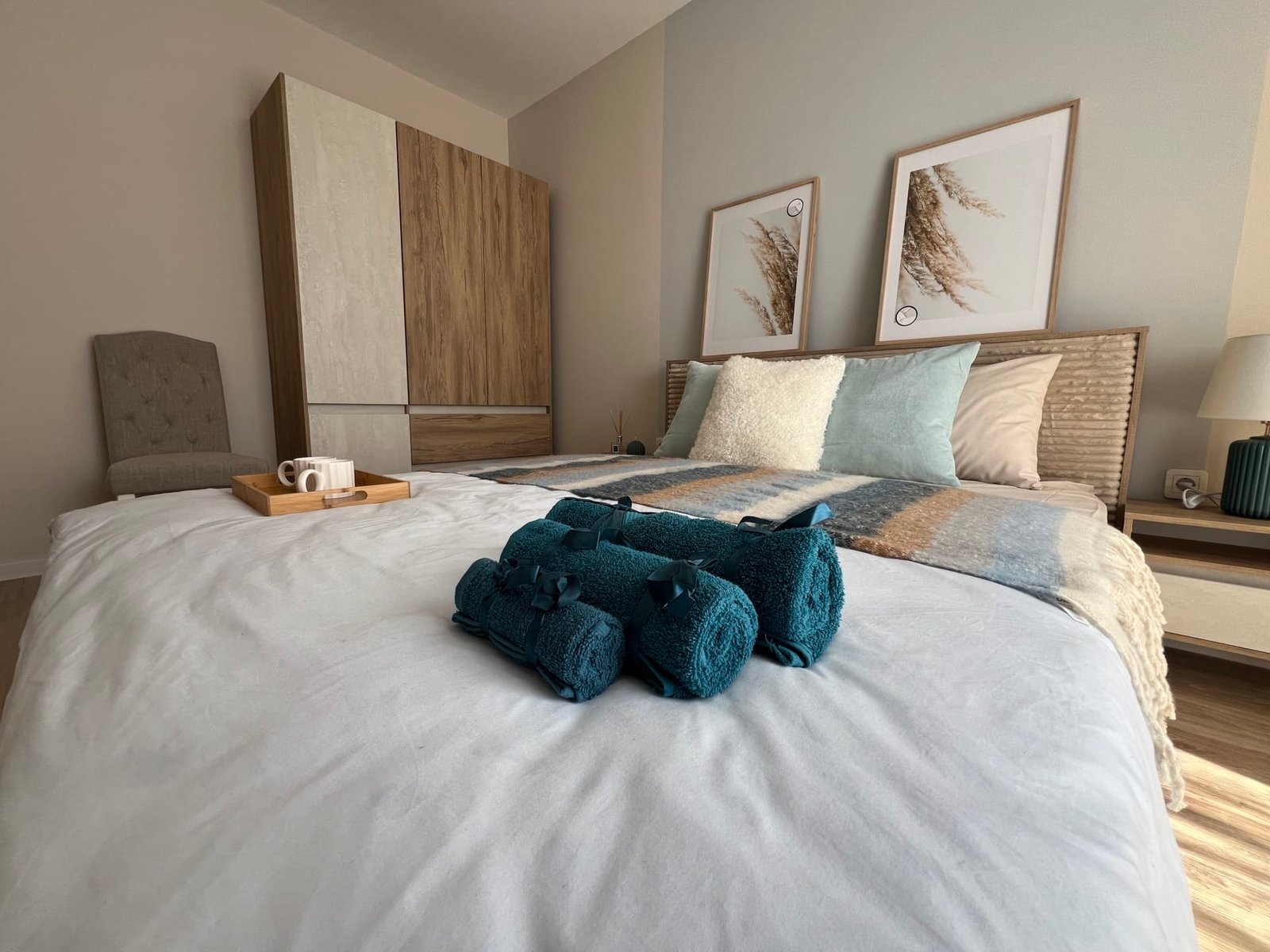 Современная спальня с уютной кроватью, декоративными подушками и стильными картинами, интерьер подходит для жилья в Болгарии.