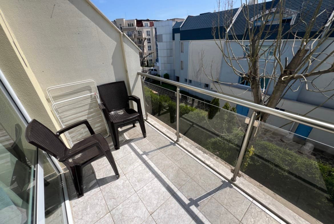 Уютный балкон с пластиковыми стульями и видом на зеленый двор в жилом комплексе Болгарии. Идеально для отдыха и наслаждения атмосферой.