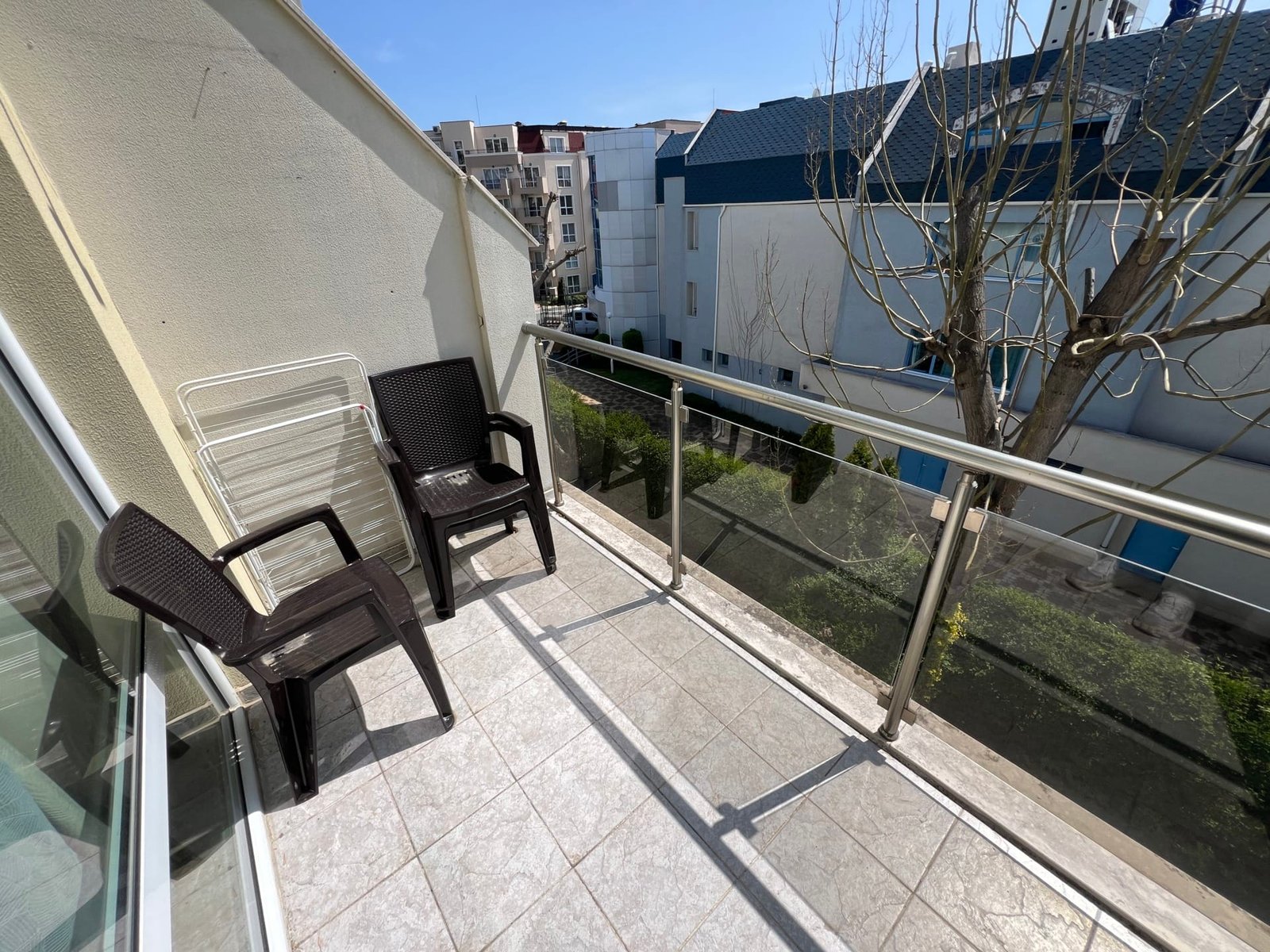 Уютный балкон с пластиковыми стульями и видом на зеленый двор в жилом комплексе Болгарии. Идеально для отдыха и наслаждения атмосферой.