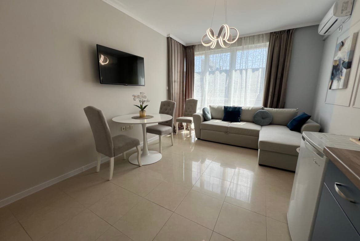 Современная гостиная в квартире в Болгарии с уютным диваном, обеденной зоной и телевизором, идеальная для покупки недвижимости.