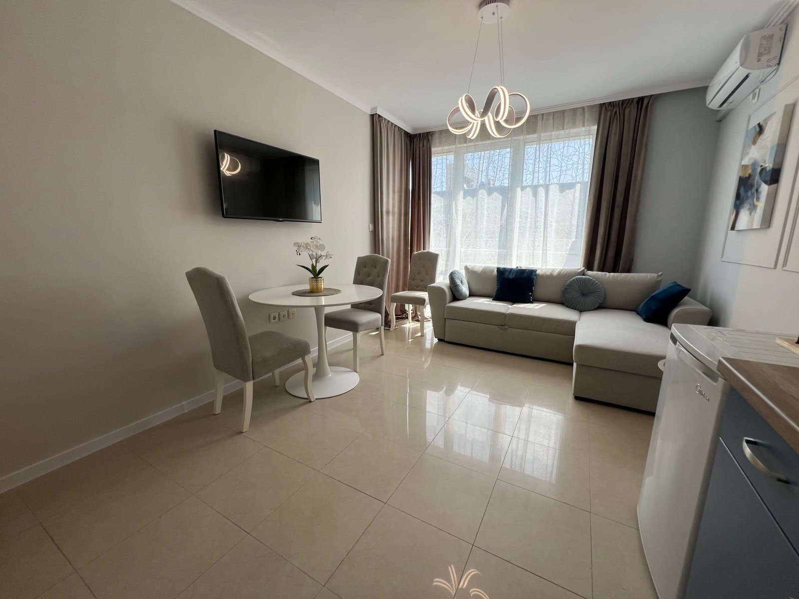 Современная гостиная в квартире в Болгарии с уютным диваном, обеденной зоной и телевизором, идеальная для покупки недвижимости.