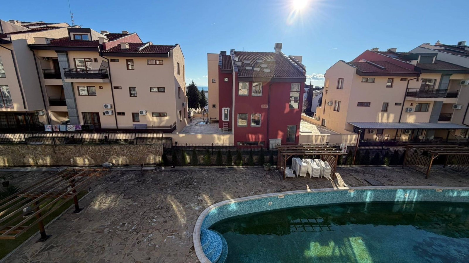 Комплекс современных жилых зданий с бассейном на фоне ясного неба в Болгарии, идеальный для покупки недвижимости.