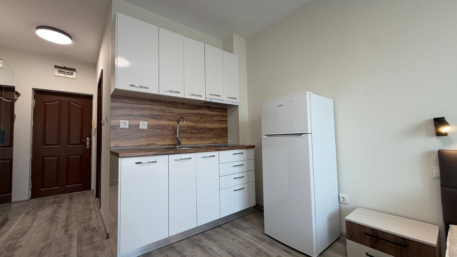 Современная кухня с белыми шкафами и деревянной столешницей, холодильником и моечными принадлежностями в квартире в Болгарии.