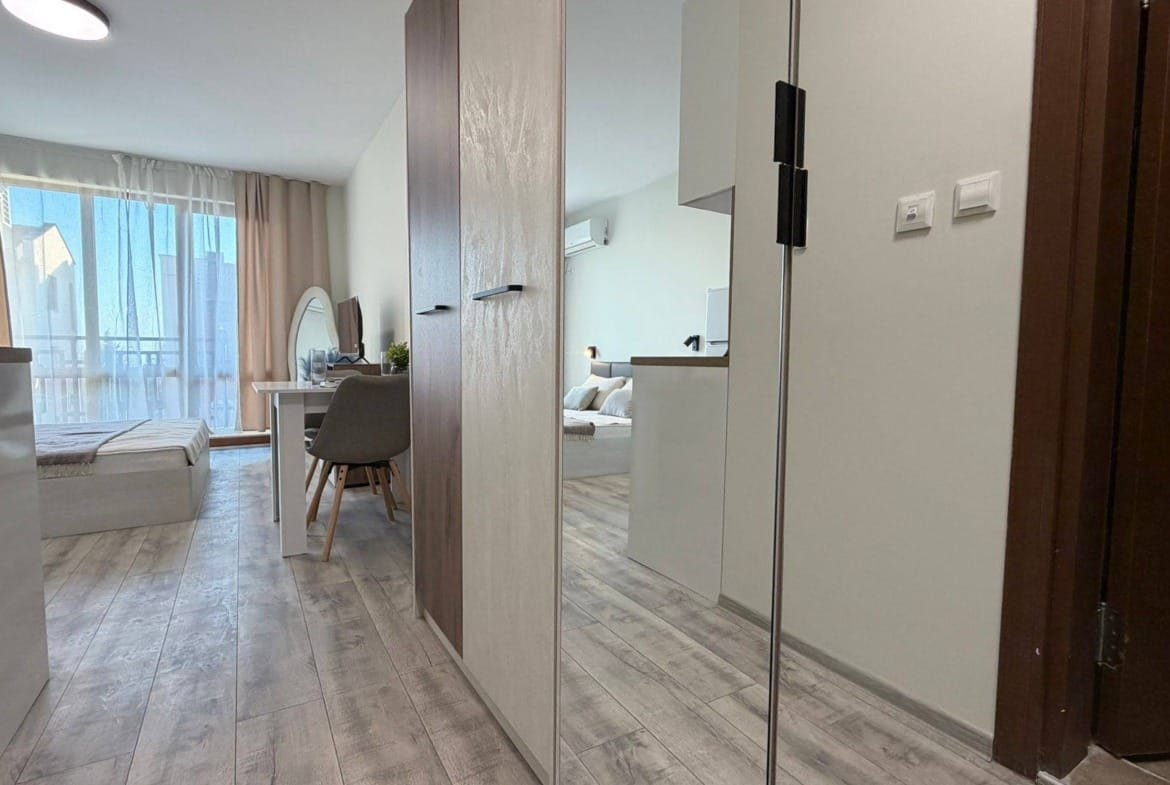 Современный интерьер квартиры в Болгарии с светлыми тонами, уютной мебелью и большим окном, создающим атмосферу комфорта.