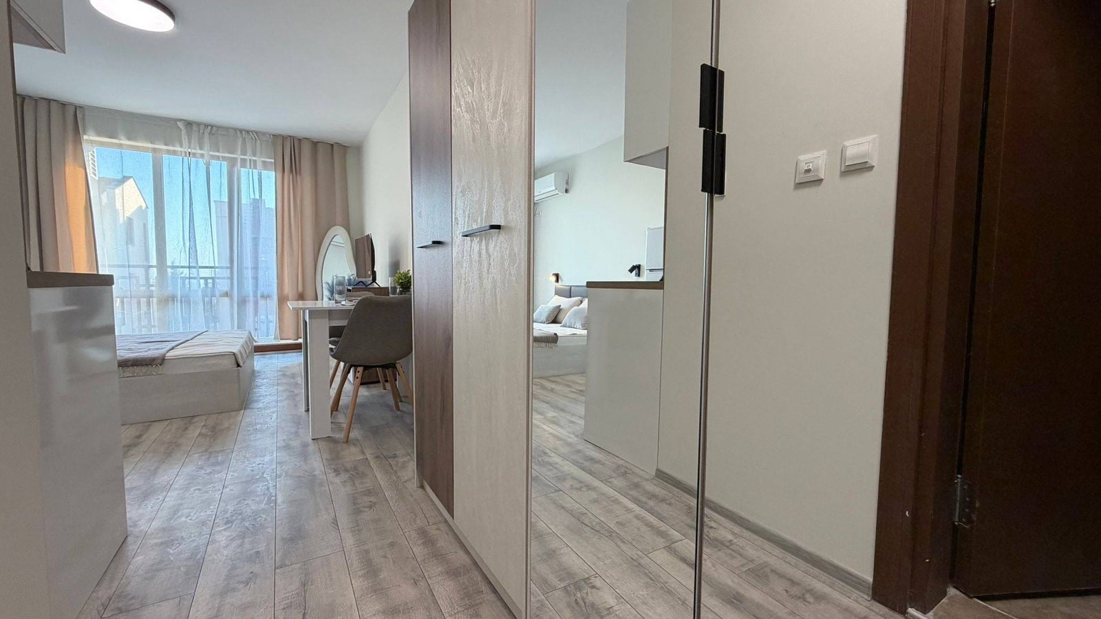 Современный интерьер квартиры в Болгарии с светлыми тонами, уютной мебелью и большим окном, создающим атмосферу комфорта.