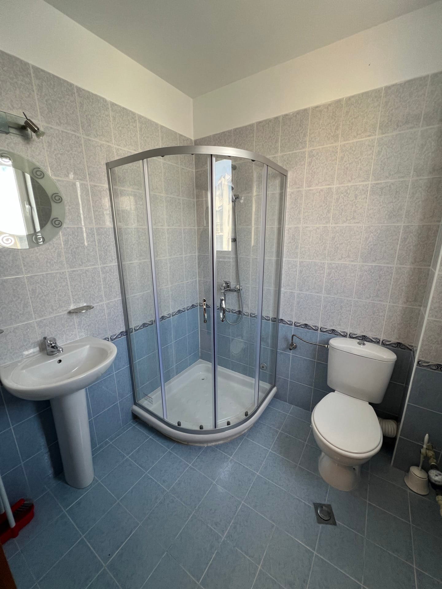 Современная ванная комната с душевой кабиной, раковиной и туалетом, отделанная голубой плиткой, идеальна для жилья в Болгарии.