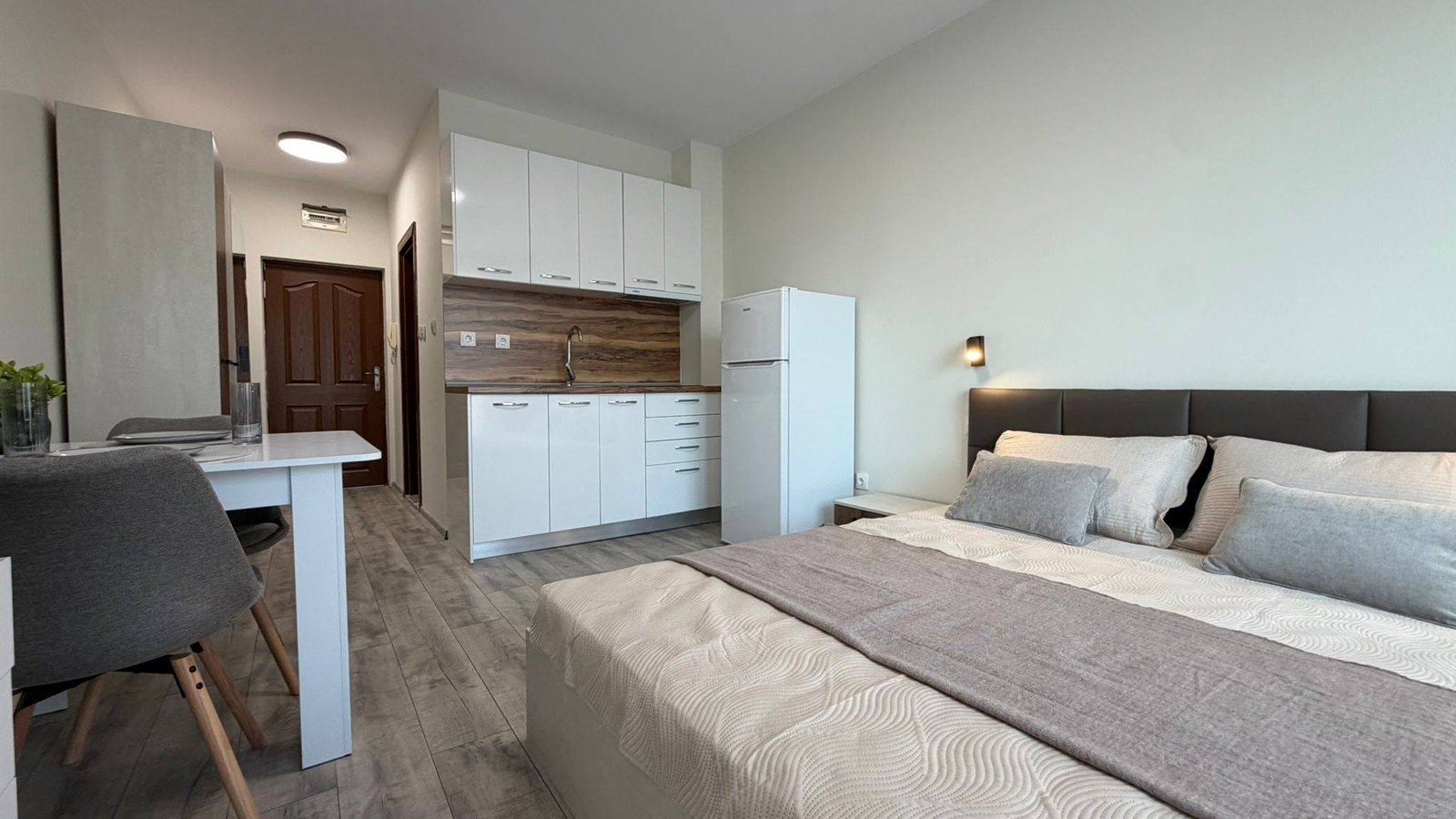 Современная студия с кухонным уголком, обеденным столом и спальней в нейтральных тонах, идеально подходит для жизни в Болгарии.