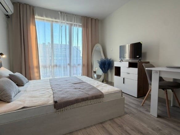 Современно оформленная спальня с двуспальной кроватью, телевизором, столом и светлыми занавесками, популярная для аренды в Болгарии.