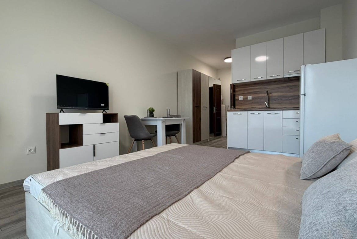 Современная однокомнатная квартира в Болгарии с кухней, кроватью, телевизором и столом, идеально подходит для комфортного проживания.